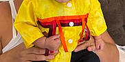 Waylon is registered to the contest to win money with this photo: baby, child, adult, yellow_shirt, ribbons, smiling, happy, indoor, sitting, person, glasses, hair, hand, feet, couch, white_tank_top, gray_pants, closeup, portrait, family