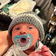 Rowan is registered to the contest to win money with this photo: baby, newborn, pacifier, knitted_hat, clothing, infant, closeup, hand, person, face, indoors, soft_light, nursery, blanket, sleepwear, cute, tiny, human, newborn_clothes, baby_hands