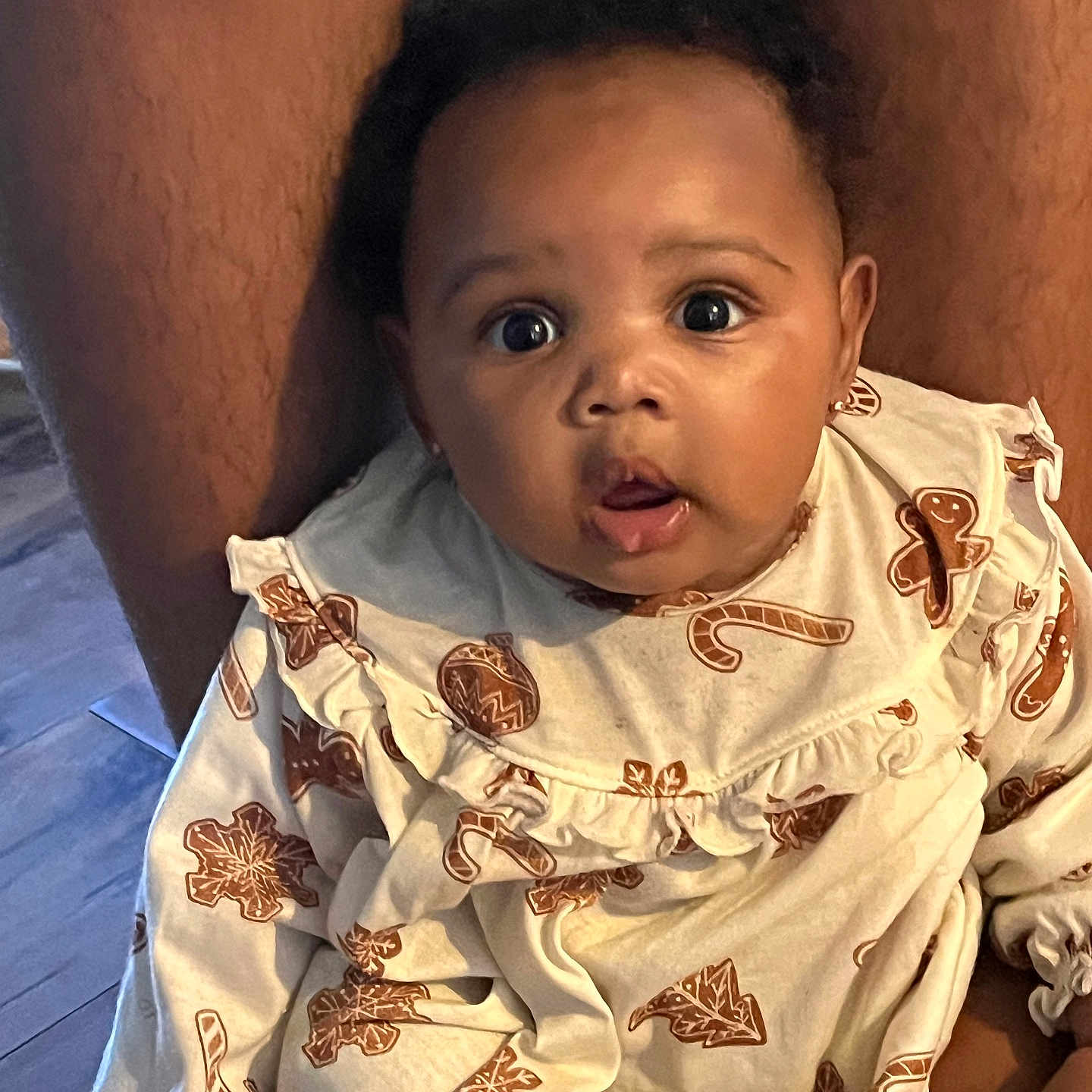 Jaliyah is registered to the contest to win money with this photo: baby, child, infant, face, person, clothing, pattern, gingerbread_man, candy_cane, holiday, festive, sitting, expression, wide_eyes, indoor, lap, skin, curly_hair, earrings, portrait