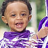 toddler, child, smiling, cheerful, pom_poms, curly_hair, purple_clothing, close_up, face, happy, outdoor, person, young_child, joyful, portrait, candid, expression, excitement, celebration, fun