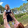 baby, casual_clothing, child, daylight, family, fence, grass, happy, holding, joy, nature, outdoor, person, playing, red_hair, sky, smiling, tattoo, trees, woman