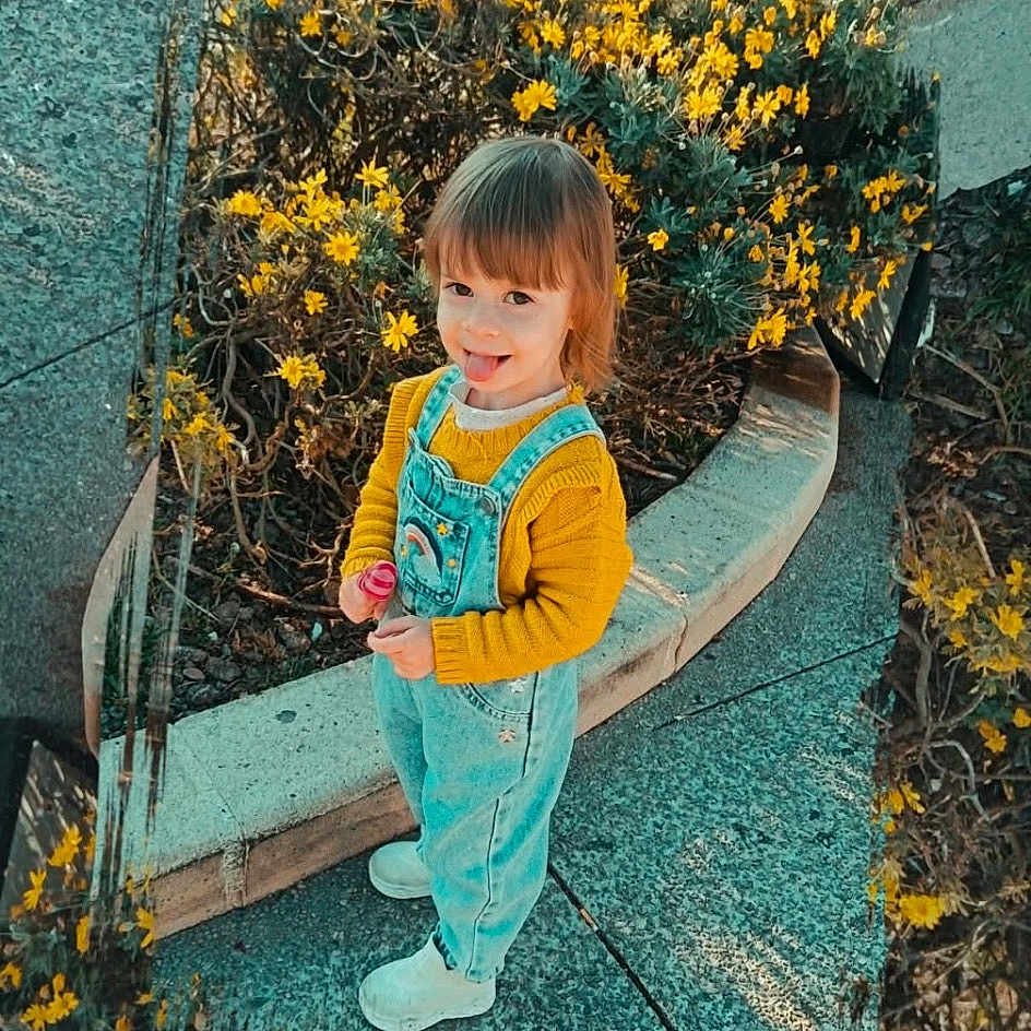 Kyara a rejoint le concours — aidez-le/la à gagner de superbes lots ! child, toddler, yellow_flowers, overalls, denim, playful, outdoor, sidewalk, curved_path, reflection, nature, happy, tongue_out, casual_clothing, daylight, greenery, shoes, young_child, smiling, flower_bed