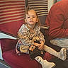 child, girl, train, seat, stuffed_toy, clothing, socks, shoes, person, window, travel, public_transport, striped_seat, red_seat, casual, indoor, young_child, portrait, serious_expression, waiting