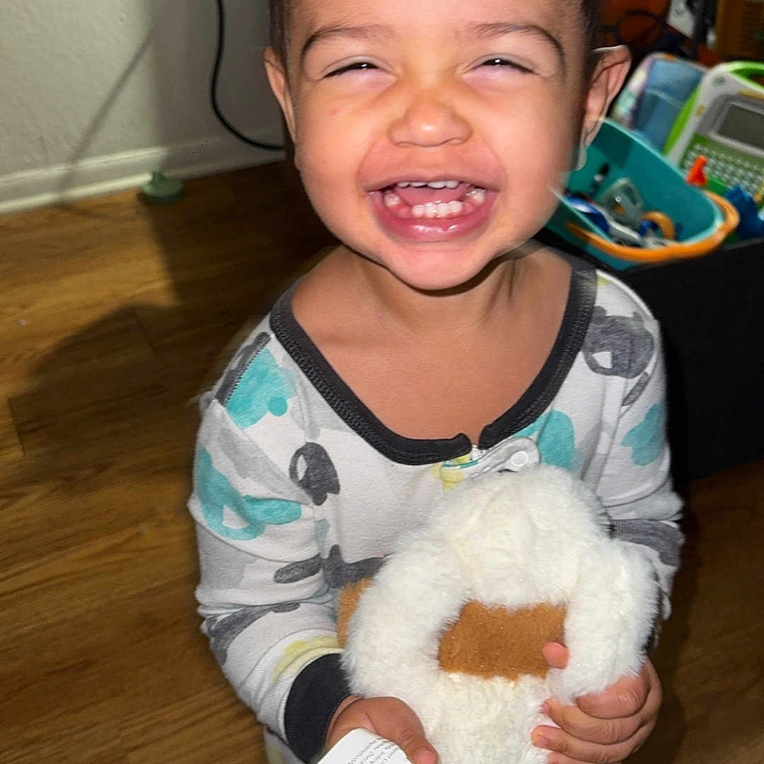 Nathaniel is registered to the contest to win money with this photo: child, cute, expression, face, happy, holding, home, indoor, joyful, pajamas, person, playroom, small_child, smiling, standing, stuffed_animal, toddler, toy, wooden_floor, young_child
