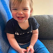 Creed joined the competition — help win amazing prizes! toddler, child, smiling, happy, indoor, couch, black_tshirt, blue_pants, toy, blanket, face, hair, hands, sitting, person, casual_clothing, playful, cheerful, home, young_child