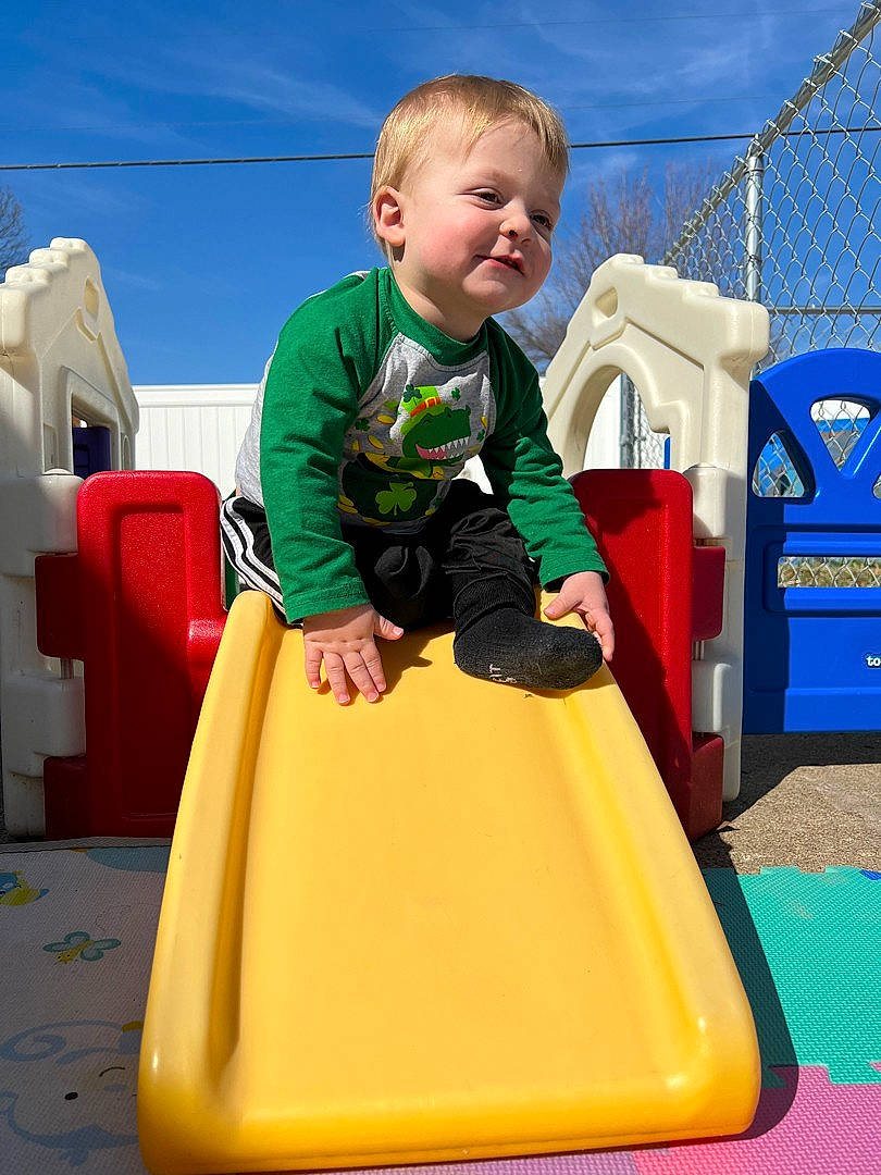 Tatum is registered to the contest to win money with this photo: baby, baby_toddler_clothing, blue, child, chute, city, cloud, fun, leisure, outdoor_play_equipment, person, play, playground, playground_slide, recreation, sitting, sky, smile, t_shirt, toddler