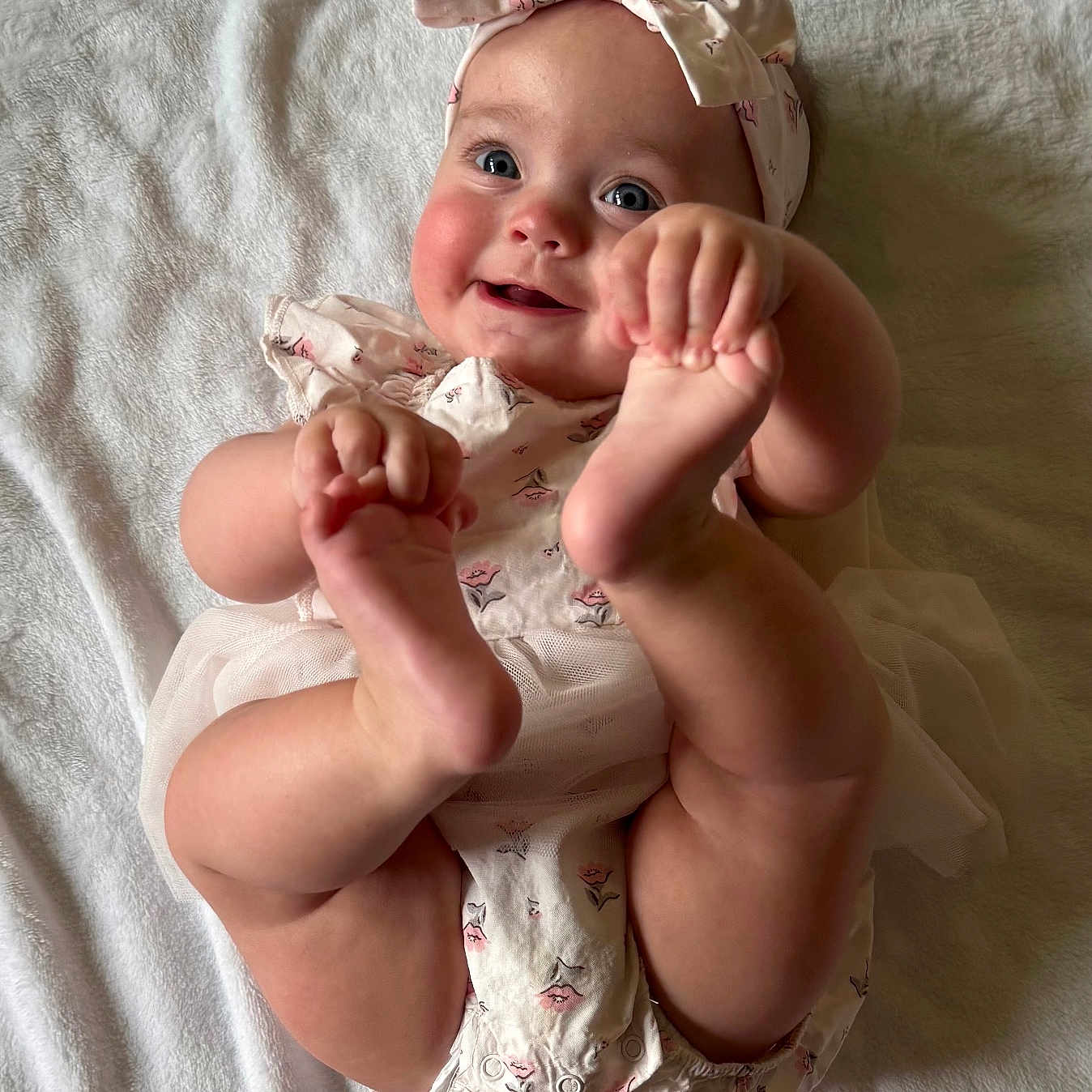 Emilia joined the competition — help win amazing prizes! baby, infant, smile, headband, barefoot, hands, feet, white_blanket, cute, portrait, child, happy, lying_down, soft_texture, skin, clothing, person, toddler, playful, indoors