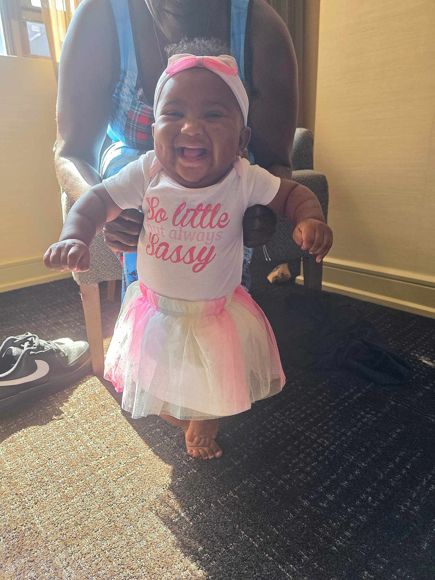 Mariah joined the competition — help win amazing prizes! baby, child, tutu, headband, smile, standing, indoor, carpet, adult_hands, footwear, shoe, sunlight, shadow, pink, white_clothing, happy, person, infant, cute, support