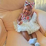 Mariah is registered to the contest to win money with this photo: baby, child, smiling, dress, tutu, headband, armchair, socks, happy, infant, cute, indoors, person, seated, plush, fabric, portrait, celebration, colorful, comfort
