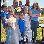 Palmer is registered to the contest to win money with this photo: family, wedding, bride, children, outdoor, sunny, blue_sky, grass, dress, bouquet, smile, casual_clothing, glasses, jeans, boots, portrait, group, celebration, happy, people
