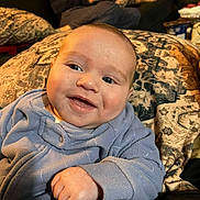 Greysen is registered to the contest to win money with this photo: baby, smiling, blue_clothing, blanket, face, hand, indoor, person, portrait, happy, couch, adult, background, cozy, relaxed, infant, closeup, expression, casual, furniture