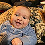 baby, smiling, blue_clothing, blanket, face, hand, indoor, person, portrait, happy, couch, adult, background, cozy, relaxed, infant, closeup, expression, casual, furniture