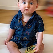 Maylon a rejoint le concours — aidez-le/la à gagner de superbes lots ! baby, child, infant, sitting, blue_clothing, short_sleeves, car_pattern, wooden_plaque, milestone, indoor, floor, feet, hands, face, eyes, hair, necklace, expression, cute, portrait