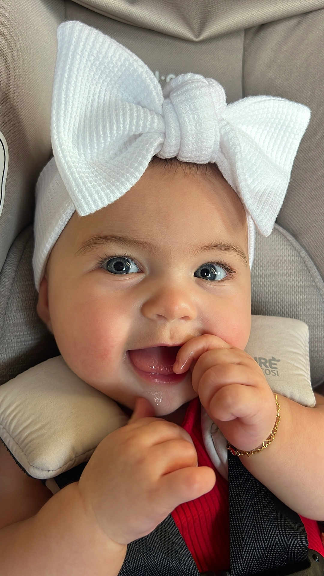 Hadley joined the competition — help win amazing prizes! baby, infant, child, smiling, happy, face, headwear, white_bow, car_seat, seatbelt, cushion, skin, hand, bracelet, red_clothing, closeup, portrait, indoors, cute, expression