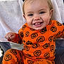 baby, chair, child, clothing, cute, face, festive, hair_clip, happy, holiday, indoors, jack_o_lantern, orange_clothing, person, portrait, pumpkin_pattern, sitting, smiling, toddler, towel