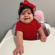 Hailey joined the competition — help win amazing prizes! baby, high_chair, red_bow, polka_dot, smiling, happy, child, infant, cute, portrait, indoor, person, toddler, hand, face, clothing, seat, pink_chair, wall, expression