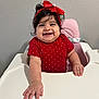 baby, high_chair, red_bow, polka_dot, smiling, happy, child, infant, cute, portrait, indoor, person, toddler, hand, face, clothing, seat, pink_chair, wall, expression