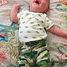 Rheis is registered to the contest to win money with this photo: baby, infant, smiling, lying_down, clothing, onesie, pants, camouflage, blanket, bed, person, happy, face, hand, footwear, indoor, cute, expression, child, resting