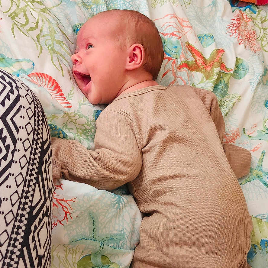 Rheis joined the competition — help win amazing prizes! baby, infant, smiling, lying_down, bedspread, onesie, cozy, cat, animal, indoor, colorful, patterned, happy, cute, person, child, fabric, pillow, home, resting