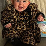 baby, infant, smile, leopard_print, coat, couch, toy, portrait, happy, cute, blue_eyes, toddler, hand, clothing, indoor, plush, sitting, face, dimple, warmth