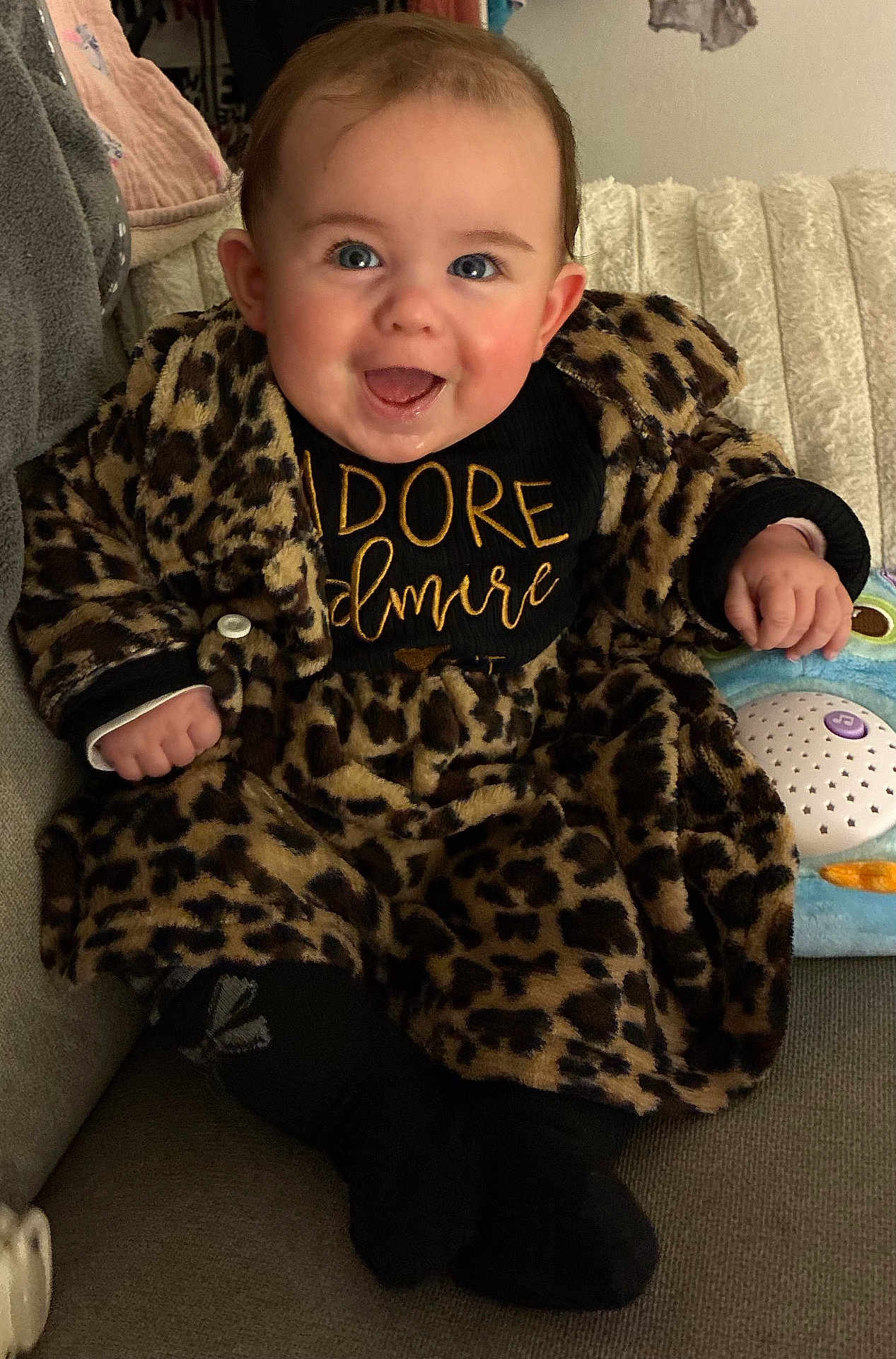 Diana a rejoint le concours — aidez-le/la à gagner de superbes lots ! baby, infant, smile, leopard_print, coat, couch, toy, portrait, happy, cute, blue_eyes, toddler, hand, clothing, indoor, plush, sitting, face, dimple, warmth