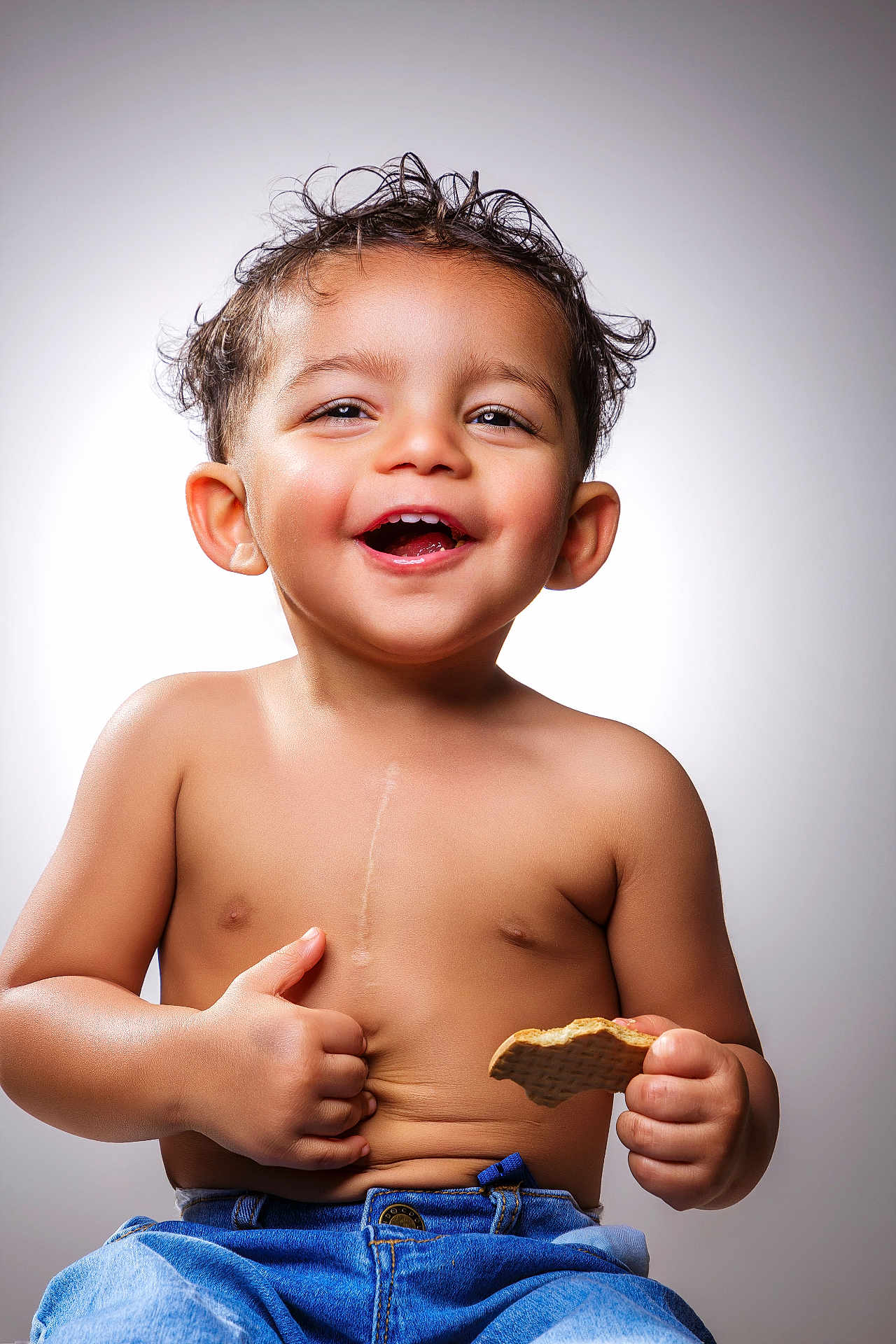 Adeen is registered to the contest to win money with this photo: toddler, child, smiling, happy, cookie, shirtless, jeans, thumbs_up, portrait, cute, baby, cute_face, short_hair, skin, hands, sitting, background, studio_light, expression, joy