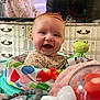 Charlotte is registered to the contest to win money with this photo: baby, smiling, red_hair, toy, activity_center, indoor, child, pacifier, green_frog_toy, colorful, face, happy, furniture, television, dressed, person, closeup, infant, cute, playtime