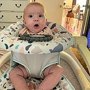 Charlotte is registered to the contest to win money with this photo: baby, infant, baby_walker, surprised_expression, indoor, furniture, dresser, legs, feet, clothing, patterned_fabric, room, door, light, floor, child, person, face, seat, toy