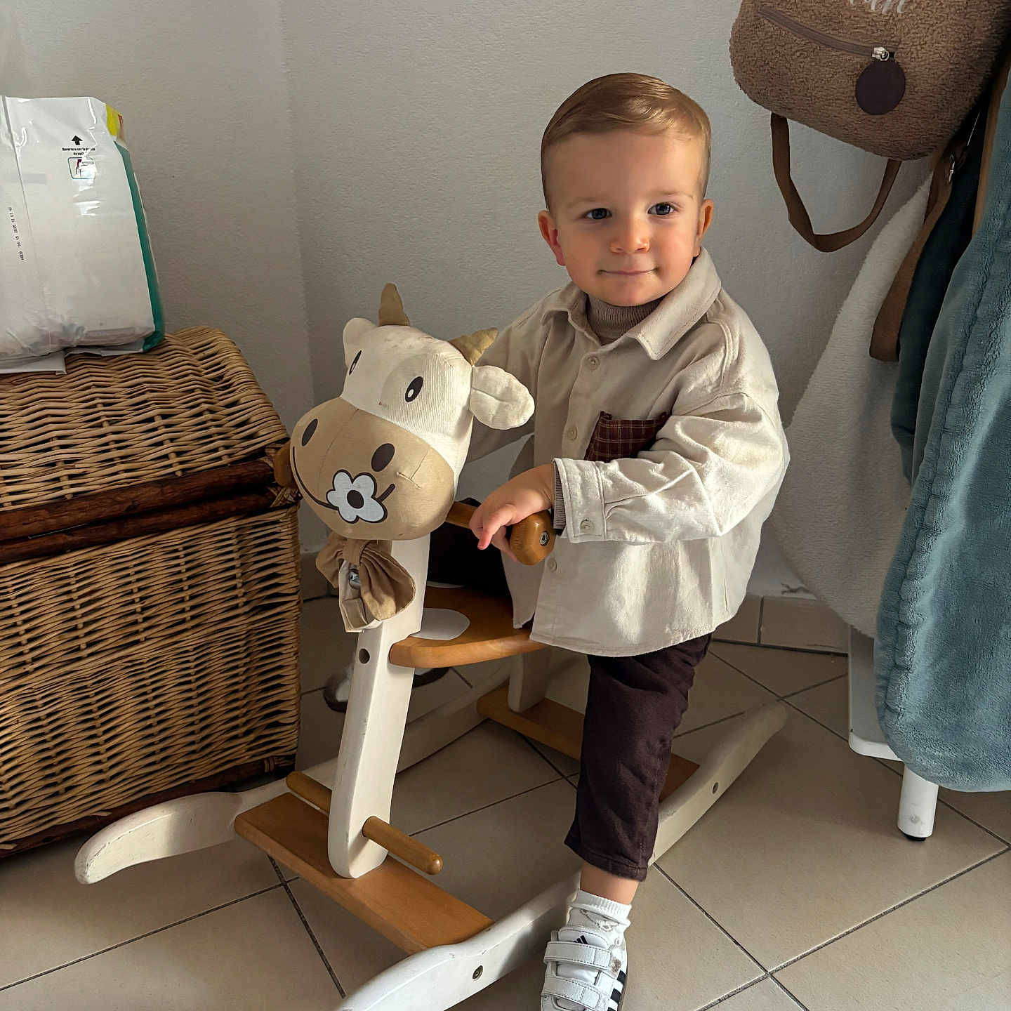 Kaelan participe au concours pour gagner de l'argent avec cette photo : baby_clothing, backpack, child, cozy, furniture, home, indoor, pants, playtime, plush_toy, portrait, rocking_horse, shirt, smile, sneakers, tile_floor, toddler, wall, wicker_basket, wooden_toy