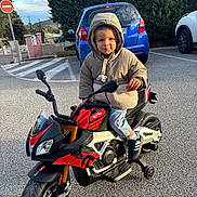 Kaelan participe au concours pour gagner de l'argent avec cette photo : child, toddler, hoodie, jacket, toy_motorcycle, aprilia, training_wheels, cookie, smile, parking_lot, blue_car, pavement, outdoor, trees, hedge, hood_up, jeans, sneakers, handlebars, no_entry_sign