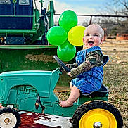Kolsyn is registered to the contest to win money with this photo: baby, child, toy_tractor, overalls, denim, camo_clothing, balloons, green, yellow, outdoor, grass, tractor, happy, smiling, barefoot, play, farm, vehicle, portrait, daytime