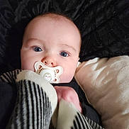 Harley is registered to the contest to win money with this photo: baby, pacifier, blue_eyes, blanket, striped_blanket, face, infant, close_up, lying_down, pillow, comfort, cute, child, soft_texture, black_background, white_pillow, sleepy, indoors, portrait, adorable
