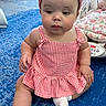 baby, child, infant, red_gingham_dress, headband, socks, blue_carpet, indoor, nursery, blanket, baby_bouncer, curious_expression, seated, cute, playful, two_babies, soft_lighting, home, floor, portrait