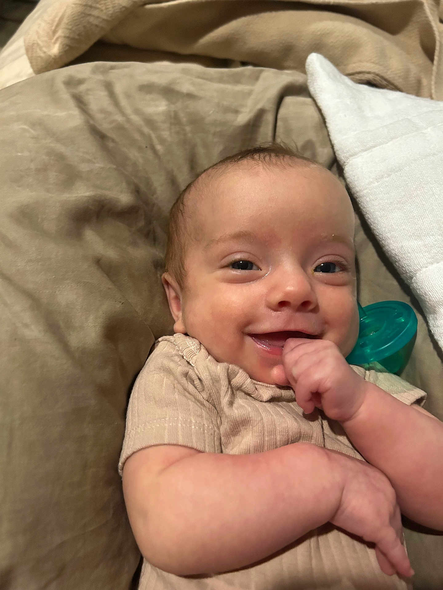 Dakota is registered to the contest to win money with this photo: baby, smile, infant, face, hand, pacifier, bed, blanket, clothing, skin, cute, child, portrait, lying_down, happy, young, indoors, comfort, closeup, expression