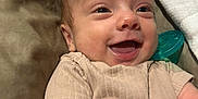 Dakota is registered to the contest to win money with this photo: baby, smiling, infant, face, happy, pacifier, clothing, beige, skin, portrait, lying_down, cute, child, newborn, human, expression, indoors, soft, warm_colors, closeup