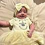 baby, bed, blanket, bow, child, clothing, cute, happy, headband, human, indoors, infant, lying_down, person, portrait, smiling, soft_lighting, toddler, tulle_skirt, yellow_dress