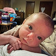 Dakota is registered to the contest to win money with this photo: baby, infant, face, hands, eyes, skin, resting, close_up, indoor, furniture, blanket, clothing, room, door, table, household, curious, portrait, newborn, expression