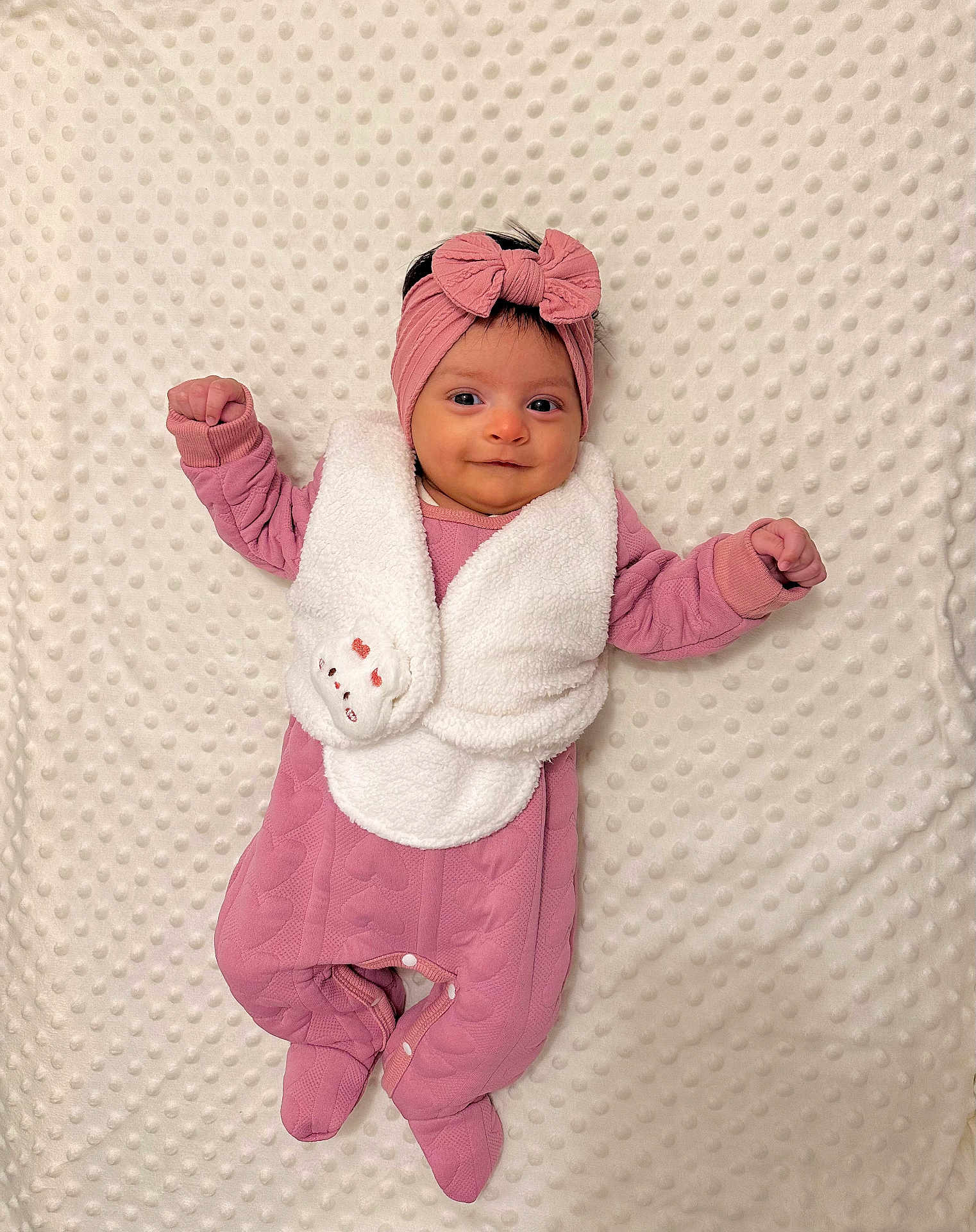 éline a rejoint le concours — aidez-le/la à gagner de superbes lots ! baby, blanket, bow, child, cozy, cute, footed_pajamas, happy, headband, indoor, infant, lying_down, newborn, pink_clothing, portrait, raised_arms, sleepwear, smiling, soft, textured_blanket