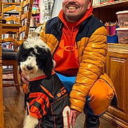 Stormy Boll joined the competition — help win amazing prizes! black_and_white_dog, books, bookshelf, chair, crouching, curly_fur, dog, fluffy, happy, home, indoor, man, orange_clothing, person, portrait, puppy, smiling, sports_jersey, wooden_floor, wooden_furniture