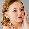 child, girl, portrait, face, close_up, smiling, curious, looking_up, brown_hair, blue_eyes, studio, gray_background, white_dress, lace, hand_on_cheek, shoulders, indoor, photography, adorable, young_child