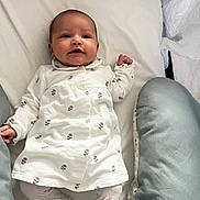 Charline participe au concours pour gagner de l'argent avec cette photo : baby, infant, newborn, onesie, floral_print, bedding, pillow, pacifier, crib, mattress, lying_down, smile, happy, face, hands, cute, cozy, portrait, white_background, home