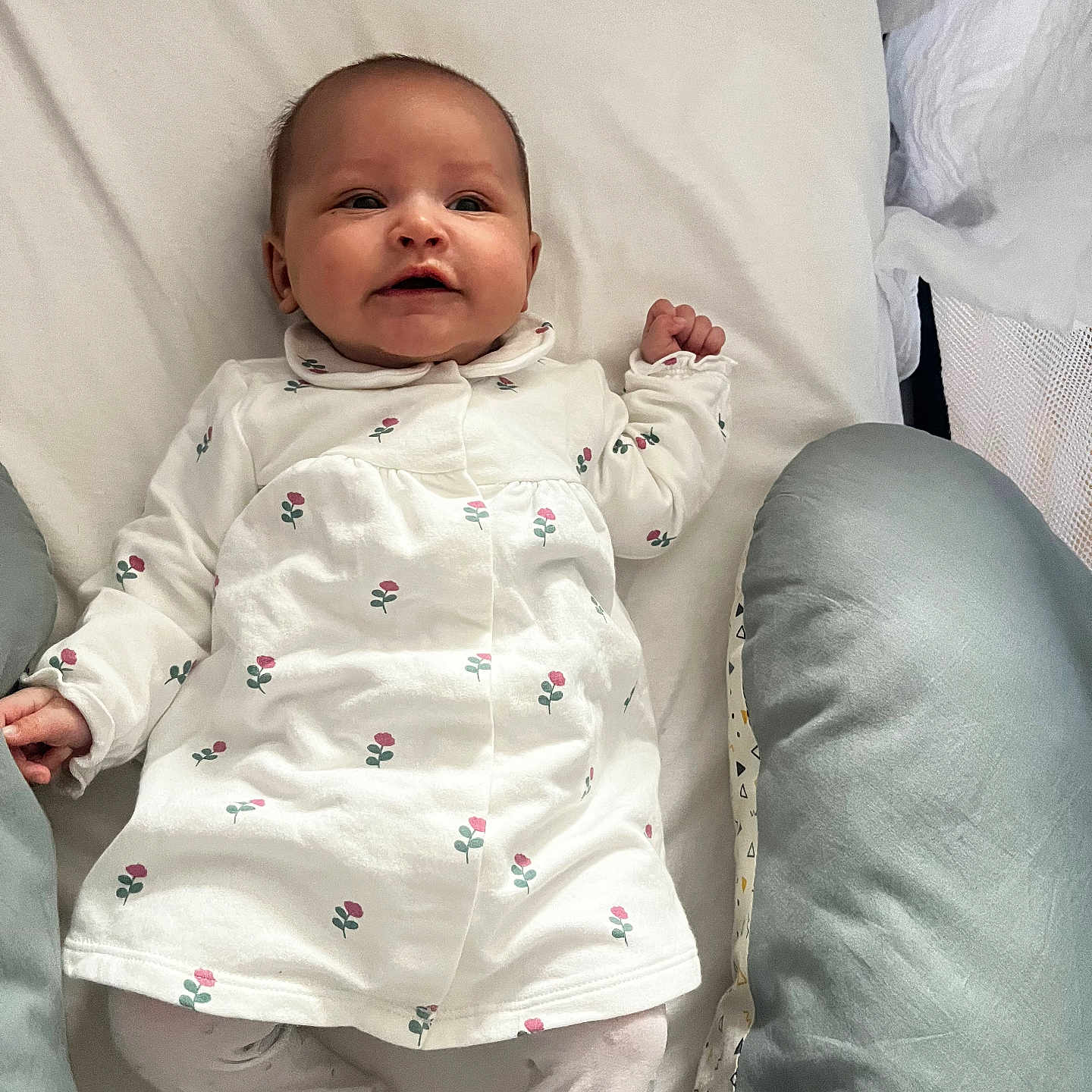 Charline participe au concours pour gagner de l'argent avec cette photo : baby, bedding, cozy, crib, cute, face, floral_print, hands, happy, home, infant, lying_down, mattress, newborn, onesie, pacifier, pillow, portrait, smile, white_background