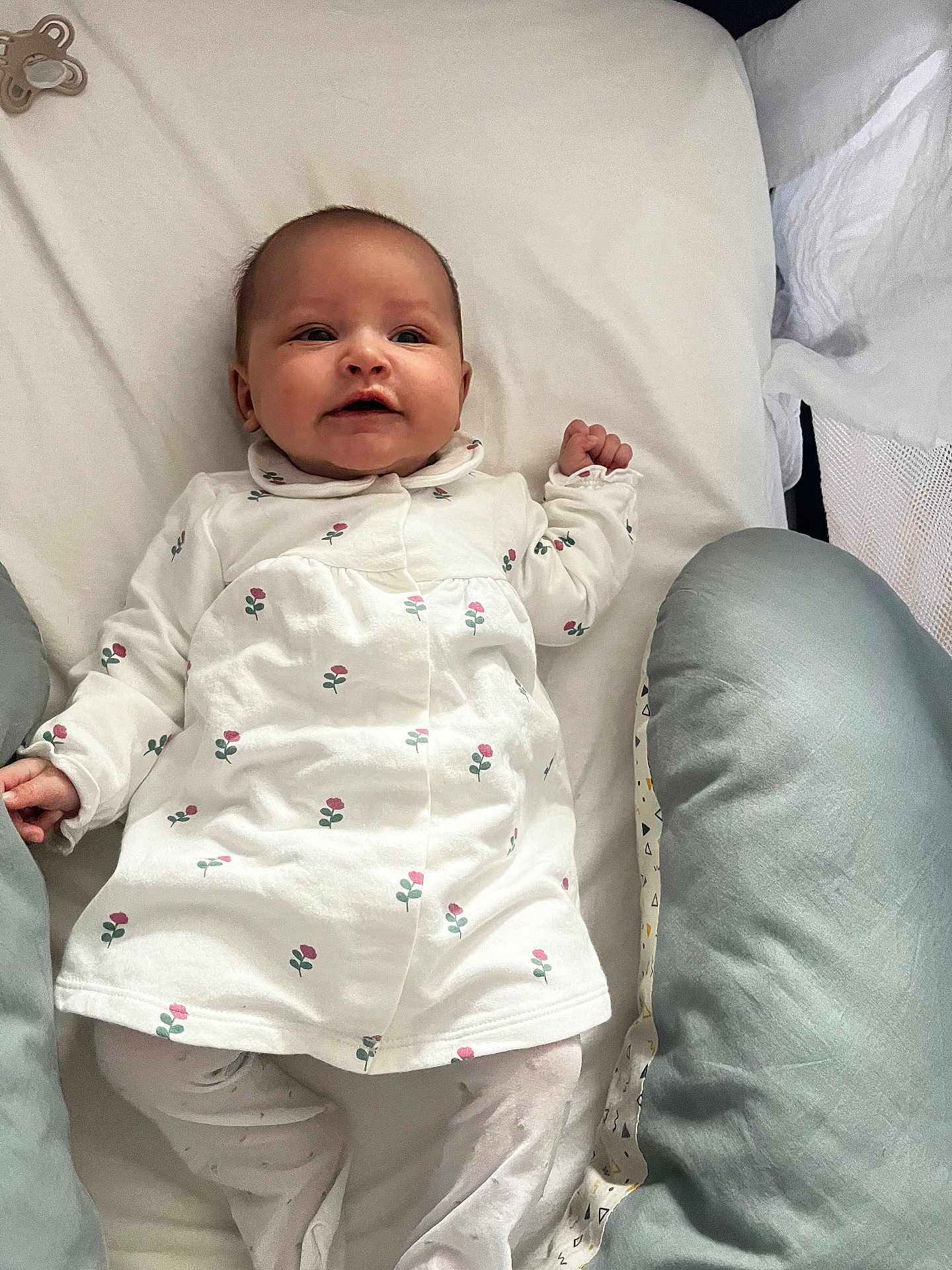 Charline participe au concours pour gagner de l'argent avec cette photo : baby, infant, newborn, onesie, floral_print, bedding, pillow, pacifier, crib, mattress, lying_down, smile, happy, face, hands, cute, cozy, portrait, white_background, home