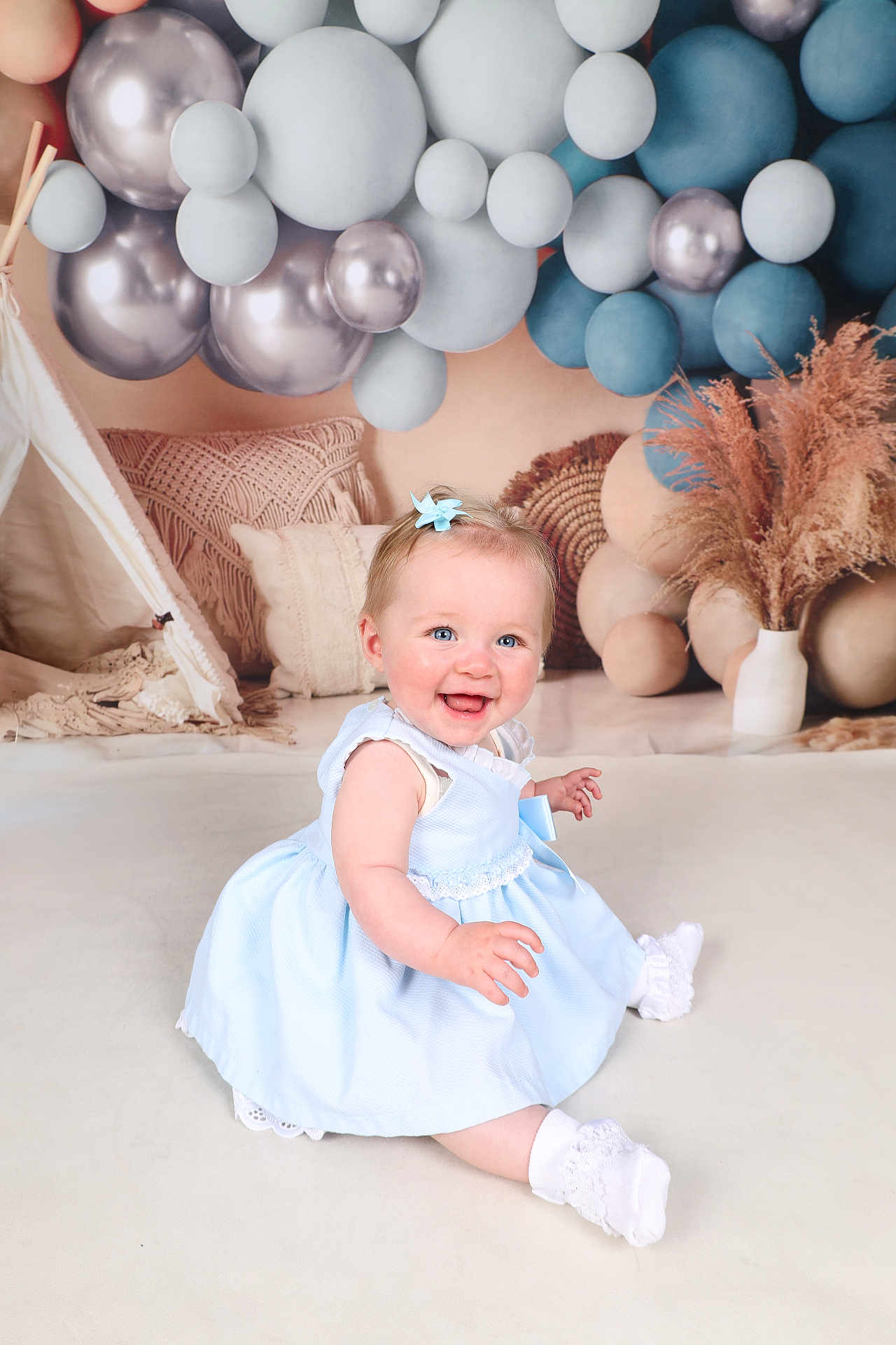 Elodie is registered to the contest to win money with this photo: baby, child, blue_dress, smiling, sitting, balloons, decor, pillow, floor, white_socks, hair_bow, cute, indoor, portrait, happy, infant, playful, soft_lighting, studio, background