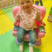 Elodie joined the competition — help win amazing prizes! baby, child, smiling, blue_eyes, bib, pink_chair, toy, play_mat, jeans, sweater, indoor, colorful, happy, cute, toddler, floor_mat, toy_phone, seat, portrait, playtime