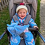 Elodie is registered to the contest to win money with this photo: toddler, stroller, child, smiling, hat, rain_suit, blue, plush_toy, outdoor, grass, fence, shoes, baby, happy, clothing, person, seat, sunny, cute, weather