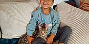 Anatol participe au concours pour gagner de l'argent avec cette photo : child, cat, sofa, cushions, blanket, indoor, smiling, happy, cozy, casual_clothing, tabby_cat, relaxed, home, comfort, cute, pet, young_child, furniture, living_room, resting