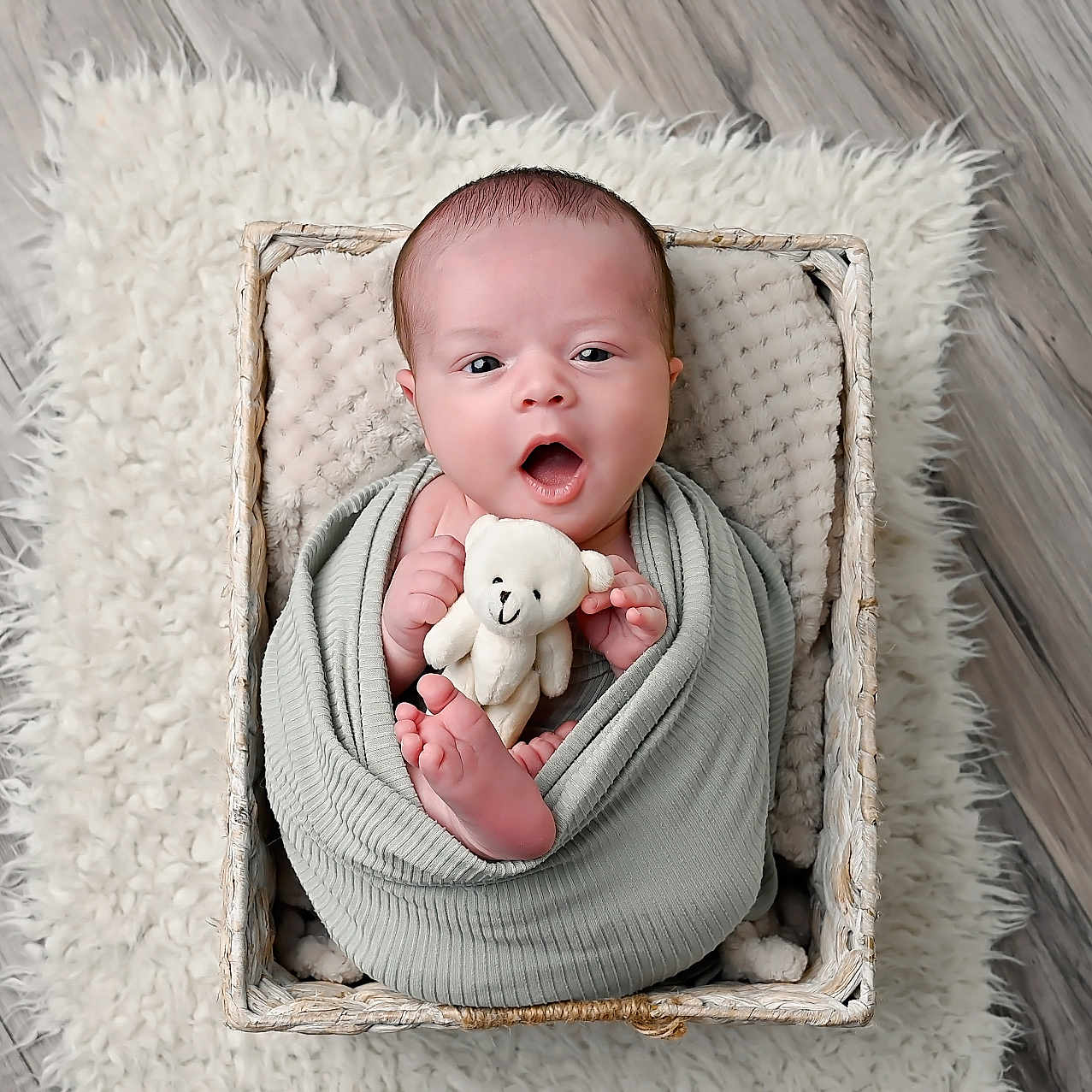 Kobe is registered to the contest to win money with this photo: baby, newborn, swaddled, basket, teddy_bear, blanket, rug, floor, cute, infant, child, portrait, soft, cozy, small, hands, feet, expression, indoor, wooden_floor