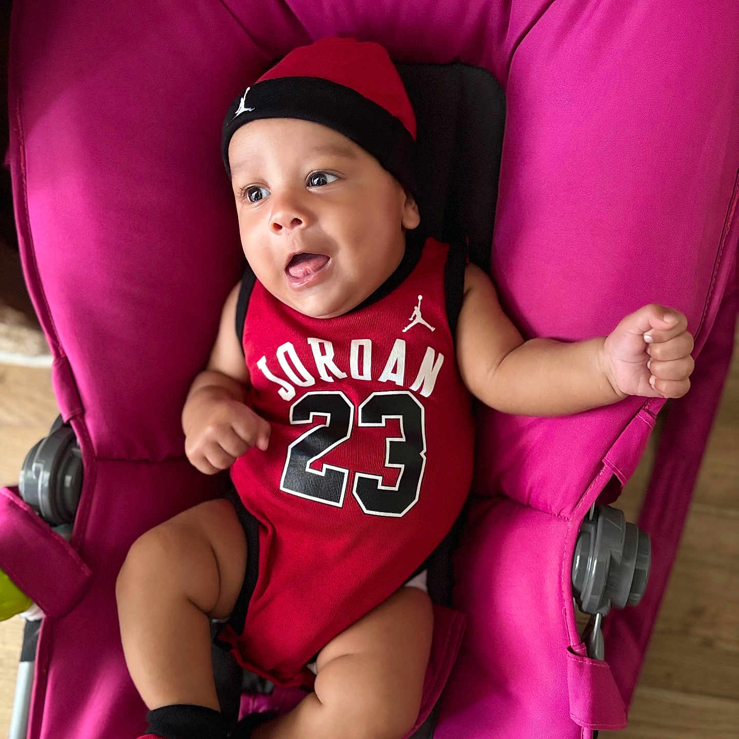 Isaiah a rejoint le concours — aidez-le/la à gagner de superbes lots ! baby, child, cute, expression, face, happy, hat, indoors, infant, jordan, person, pink, playful, portrait, red_clothing, seated, smiling, socks, stroller, young