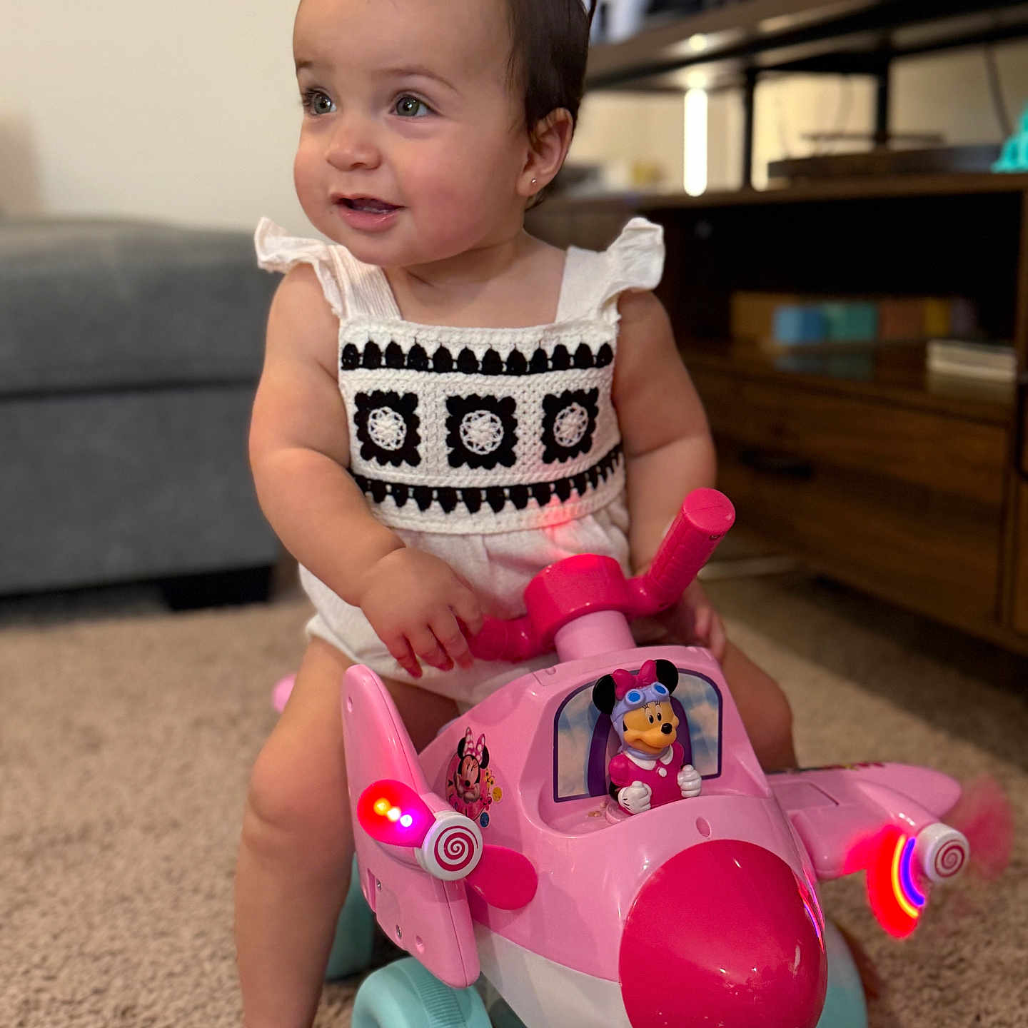 Aslihan joined the competition — help win amazing prizes! baby, carpet, child, clothing, cute, decor, foot, furniture, indoor, light, living_room, minnie_mouse, person, pink_toy, playful, short_hair, smiling, television, toddler, toy_airplane